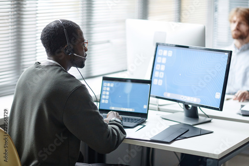 Side view portrait of Black young man wearing headset as client support operator at data security company