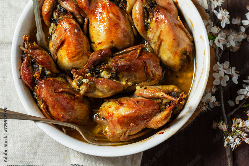 Baked quail stuffed with mushrooms, eggs and bread in a ceramic form on a wooden table.
