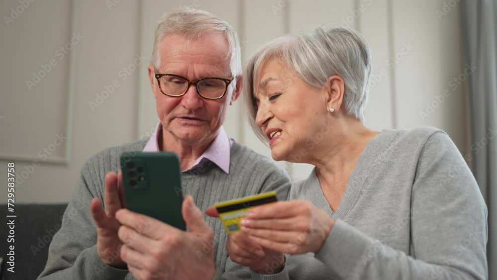 Senior couple man woman shopping online with smartphone paying with credit card. Old people buying on Internet enter credit card details at home indoors. Online shopping delivery service ecommerce Senior couple man woman shopping online with smartphone paying with credit card. Old people buying on Internet enter credit card details at home indoors. Online shopping delivery service ecommerce