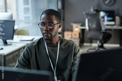 Minimal portrait of focused Black man using computer in IT development office with code lines reflection in glasses copy space