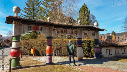 Tourist man in front of chinese style gate at church of Saint Barbara designed by architect Friedensreich Hundertwasser, Austria, Steiermark, Südwest-Steiermark, Bärnbach. Scenic artistic landmark photo