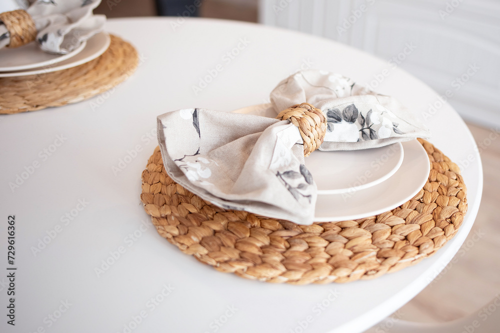 close-up of a white table set in boho style with a wicker stand and linen napkin.kitchen table close-up of a white table set in boho style with a wicker stand and linen napkin.kitchen table