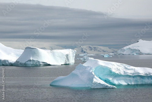 Antarctic landscape with snowy mountains, glaciers and icebergs. Landscape of icy shores in Antarctica. Beautiful blue iceberg with mirror reflection floats in ocean. Glaciers of a harsh continent
