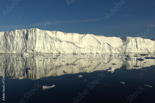 Antarctic landscape with snowy mountains, glaciers and icebergs. Landscape of icy shores in Antarctica. Beautiful blue iceberg with mirror reflection floats in ocean. Glaciers of a harsh continent