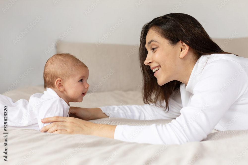 Young mother playing with her little daughter on bed, kid with mom in the morning in bedroom, child care, concept of happy motherhood Young mother playing with her little daughter on bed, kid with mom in the morning in bedroom, child care, concept of happy motherhood