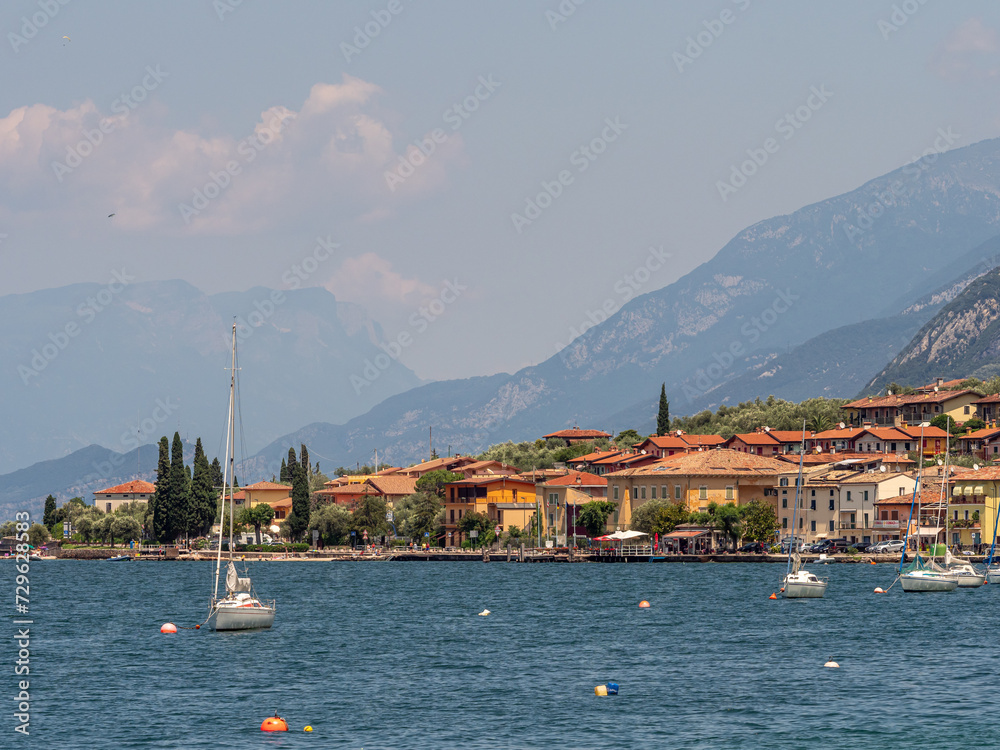 view of boats on the water and houses on the Riva di Guarda coastline, during summer, Italy.