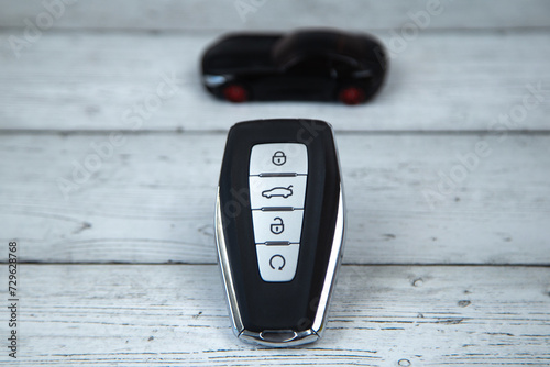 The car keys are black with metal inserts and automatic buttons on the background of white wood, on top of the keys is a black car in focus. High quality photo