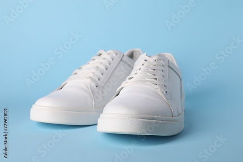Pair of stylish white sneakers on light blue background