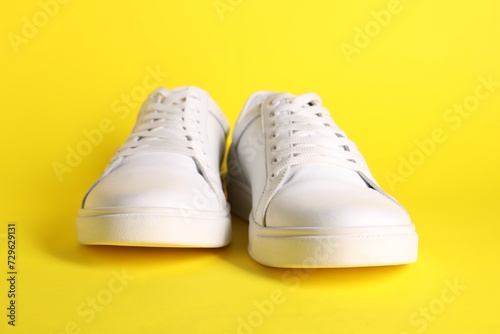 Pair of stylish white sneakers on yellow background