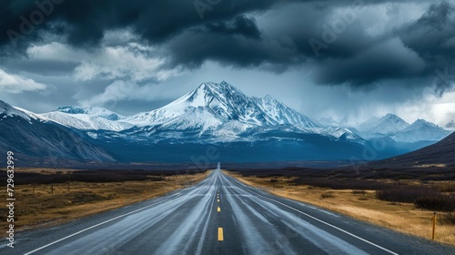  a long straight road with a mountain in the background and a cloudy sky in the middle of the road, with a yellow line in the middle of the road.