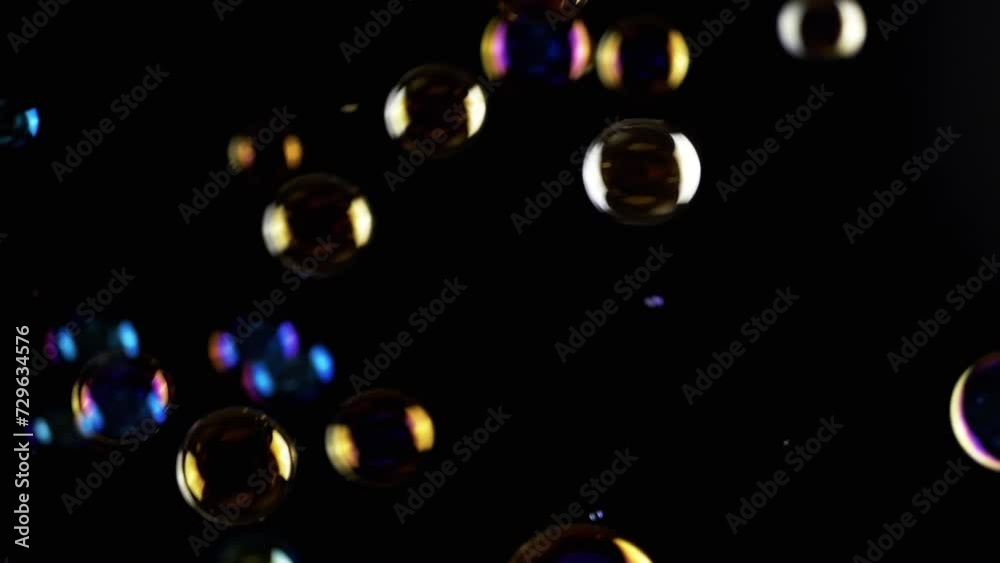 Colorful Soap Bubbles Fly in Empty Space on Isolated Black Background. Colorful lights. Many rainbow transparent bubbles randomly rotate, float, fall, burst. Blurred motion. Selective focus. Abstract. Colorful Soap Bubbles Fly in Empty Space on Isolated Black Background. Colorful lights. Many rainbow transparent bubbles randomly rotate, float, fall, burst. Blurred motion. Selective focus. Abstract.