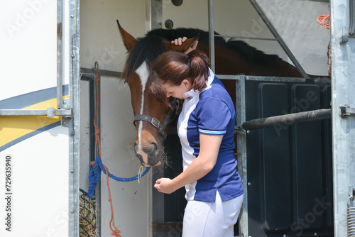 Fotografija Pretty young female rider spends a moment with her horse as it stands tried up in its horse box after competition, before driving home