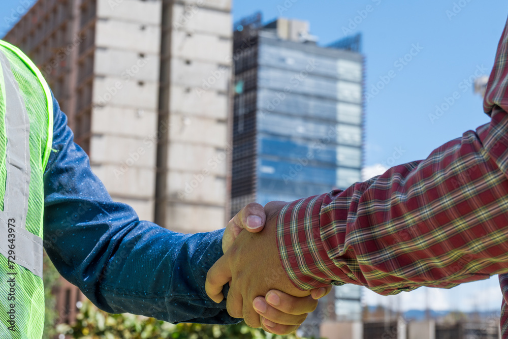 Construction workers shaking hands in construction site  in sunny day