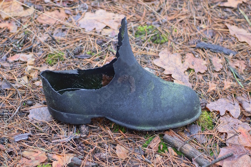 one old black torn rubber boot stands on the ground in the street