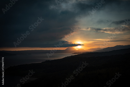 Sunrise gracing the skyline above Arenal Lake in Costa Rica, with a prominent volcano centered in the frame.