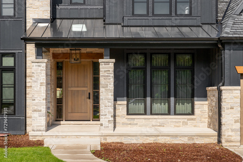 A front door detail on a home with black board and batten siding with natural stone accents and a beautiful oak front door. 