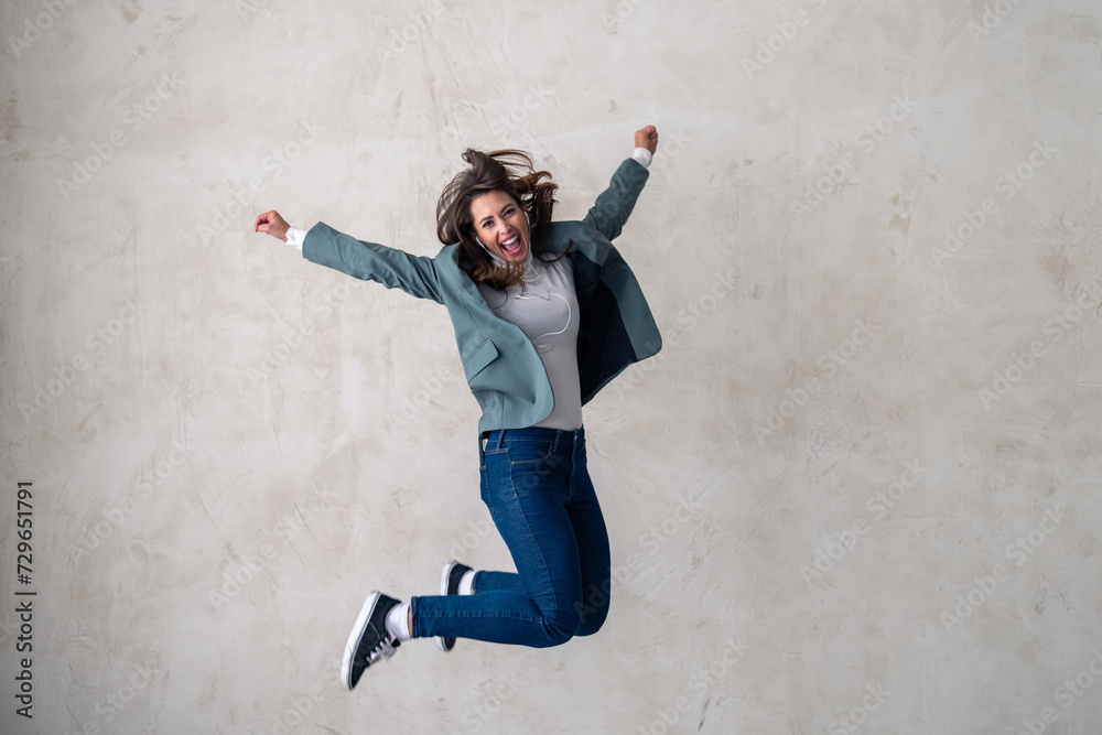 Full length shot of a happy young woman jumping into the air against a gray background.