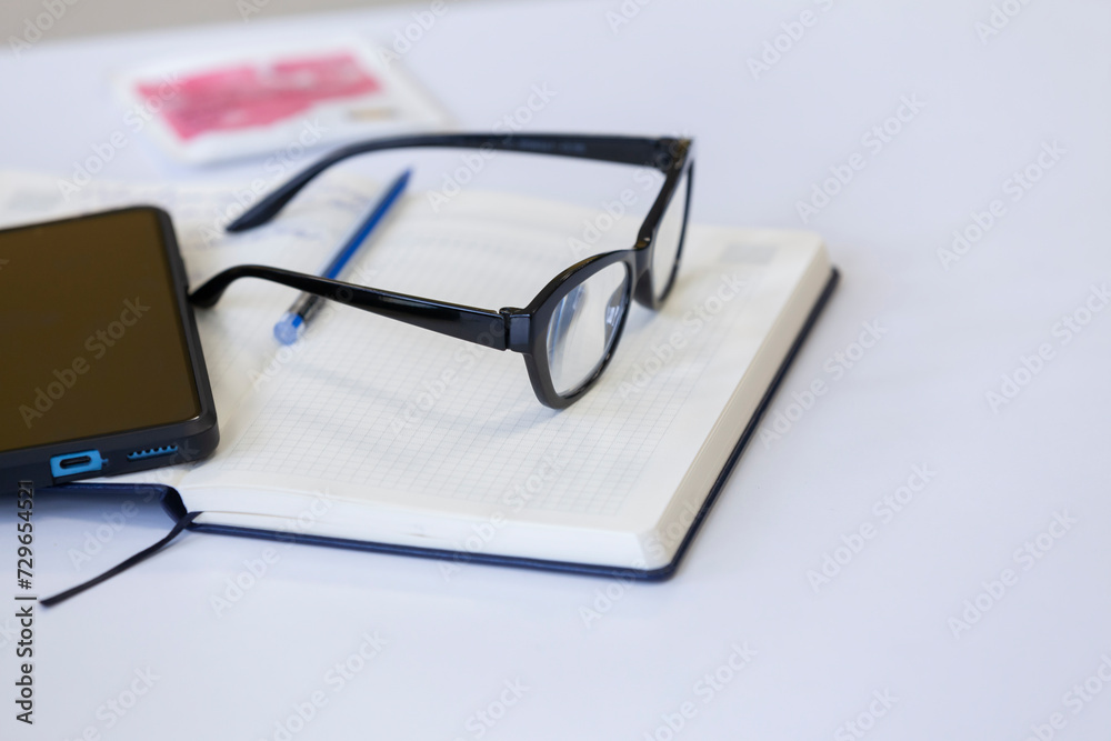 Glasses, smartphone and notepad on the desktop. Work or workplace concept.