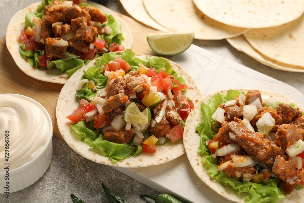Delicious tacos with vegetables, meat and lime on grey textured table Delicious tacos with vegetables, meat and lime on grey textured table