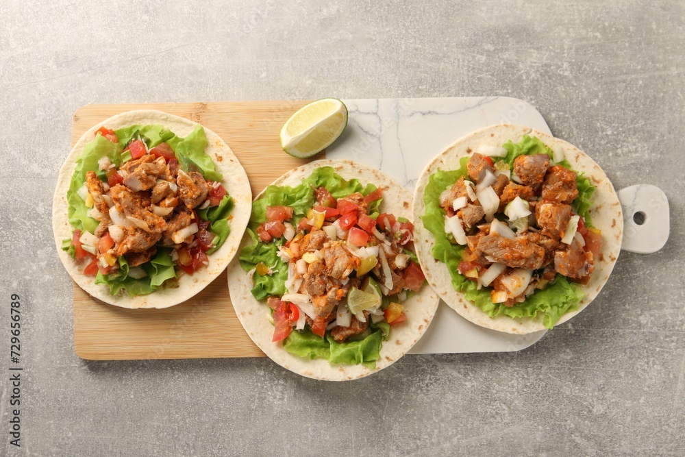 Delicious tacos with vegetables, meat and lime on grey textured table, top view