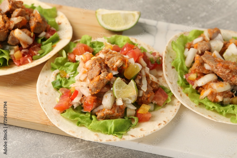 Delicious tacos with vegetables, meat and lime on grey textured table, closeup Delicious tacos with vegetables, meat and lime on grey textured table, closeup