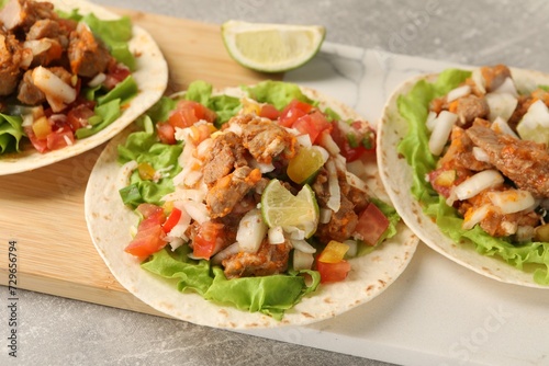 Delicious tacos with vegetables, meat and lime on grey textured table, closeup