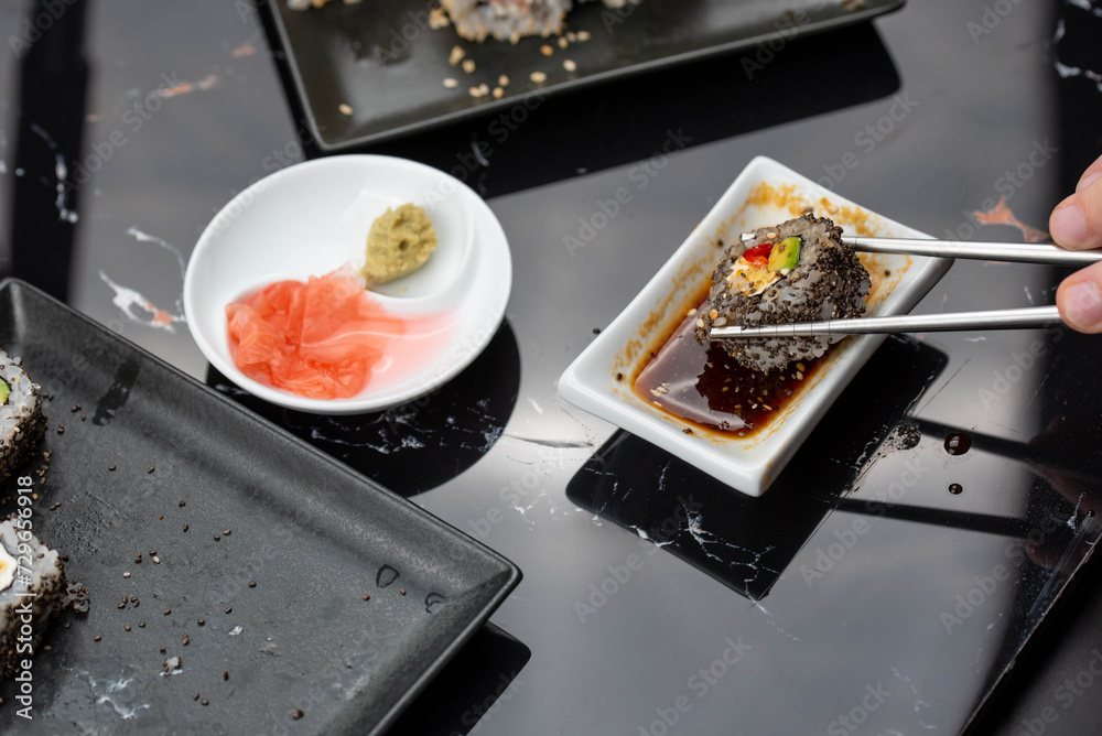 Close up of hands with chopsticks eating japanese food. Traditional asian rolls. Maki sushi with vegetables and tuna Close up of hands with chopsticks eating japanese food. Traditional asian rolls. Maki sushi with vegetables and tuna