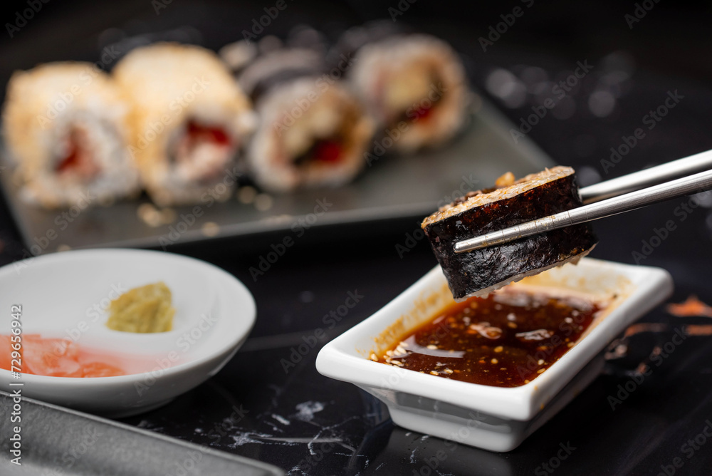 Close up of hands with chopsticks eating japanese food. Traditional asian rolls. Maki sushi with vegetables and tuna