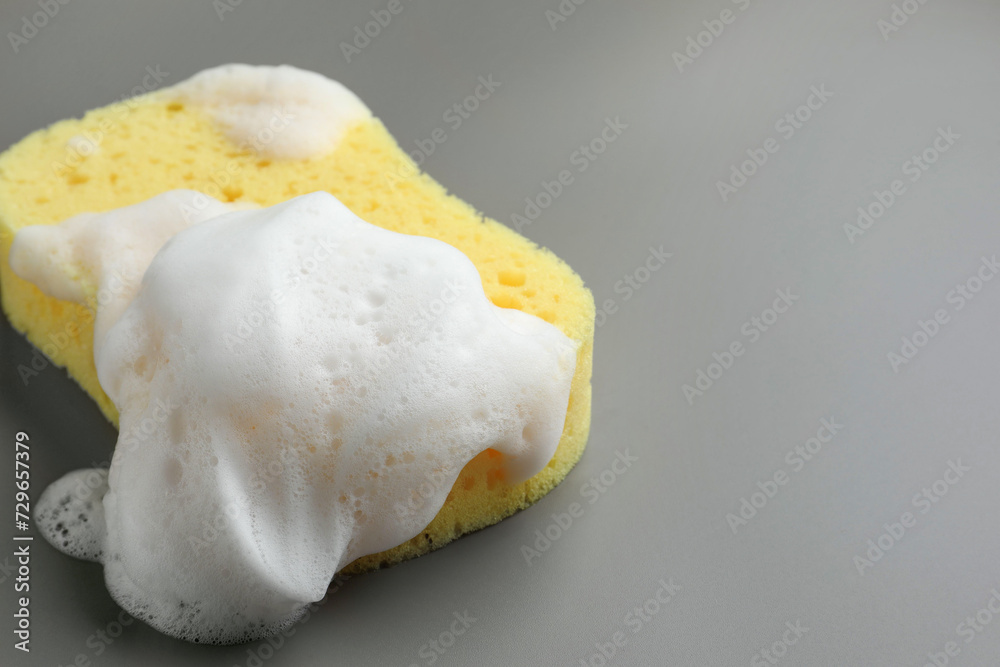 Yellow sponge with foam on grey background, closeup