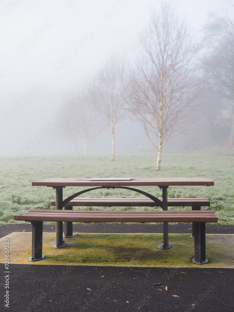 Modern metal bench and table with plastic elements in a park, fog in the background over green field. Surreal mood. Calm nature scene with mist