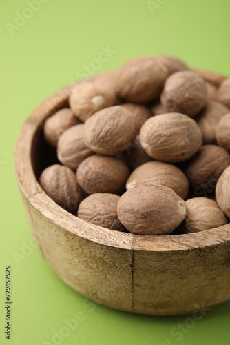 Whole nutmegs in bowl on light green background, closeup