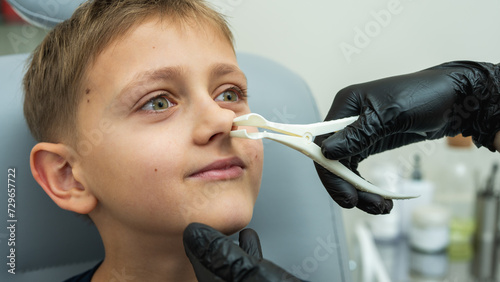 examination and examination of the nose, little boy, fair-haired teenager smiling, sitting in the otolaryngologist's office, examining the nasal passages at the doctor, trusting, emotional, smiling.  photo