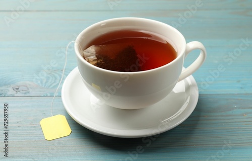 Tea bag in cup with hot drink on light blue wooden table, closeup