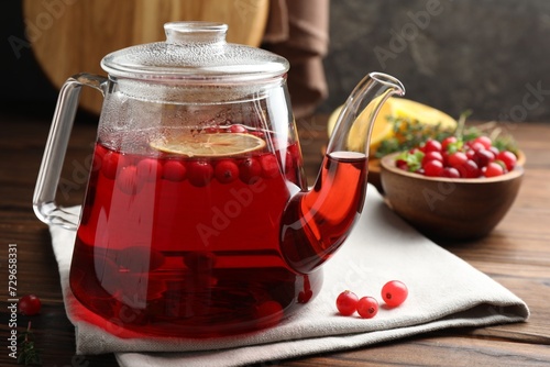 Tasty hot cranberry tea in teapot and fresh berries on wooden table