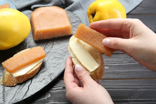 Woman making sandwich with quince paste at black wooden table, closeup photo