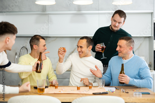 Friends drinking beer and enthusiastically playing a board game at home
