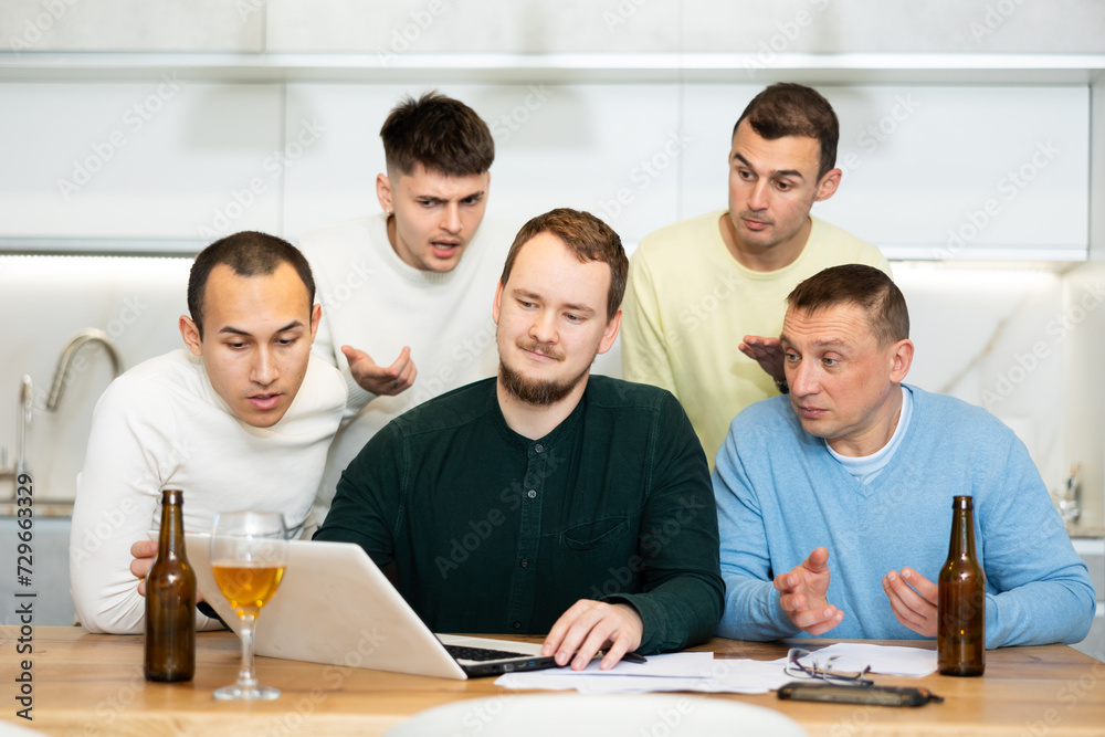 Group of male friends solving problems using laptop and drinking beer at home