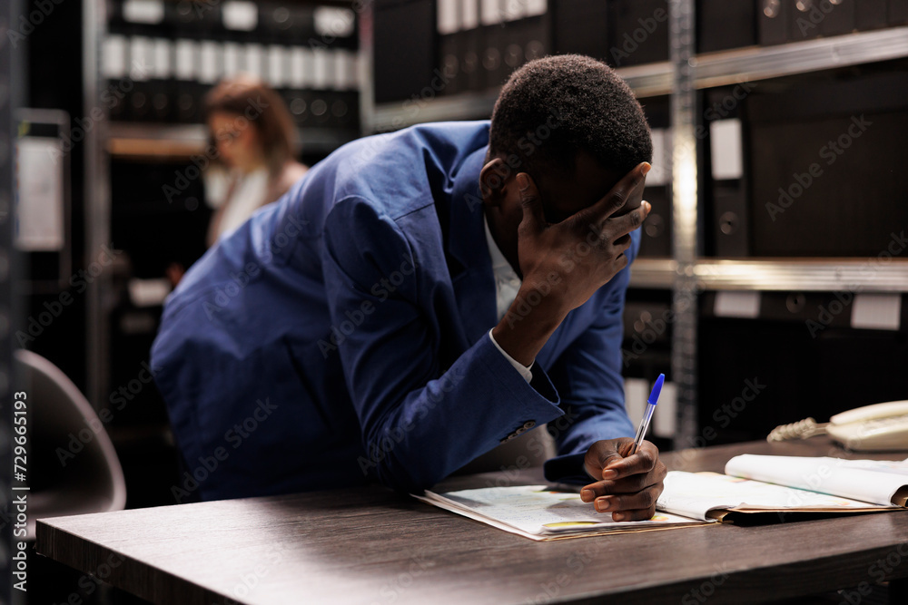African american inspector thinking at ideas to solve criminal case, analyzing investigation report. Private detective searching for criminology evidence, working overtime in arhive room.