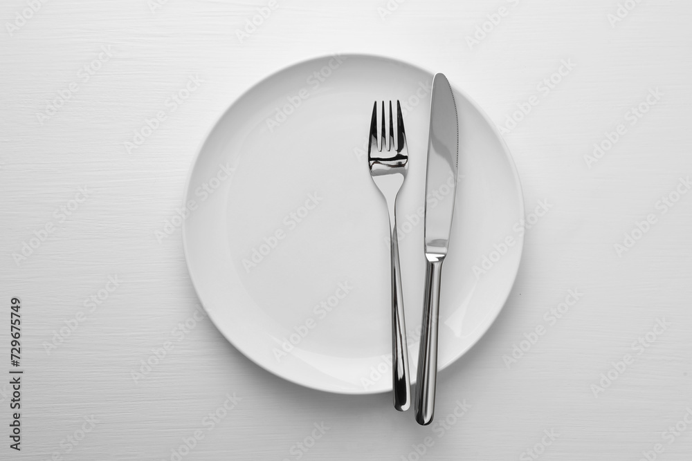 Clean plate, fork and knife on white table, top view Clean plate, fork and knife on white table, top view