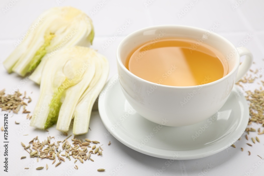 Fennel tea in cup, seeds and fresh vegetable on white tiled table, closeup Fennel tea in cup, seeds and fresh vegetable on white tiled table, closeup