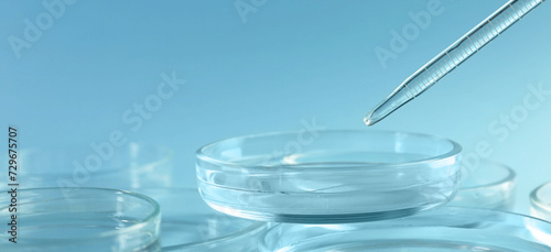 Pipette over petri dish on light blue background, closeup
