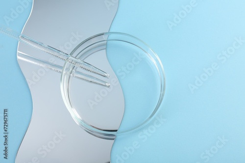 Empty petri dish, pipette and mirror on light blue background, flat lay. Space for text photo