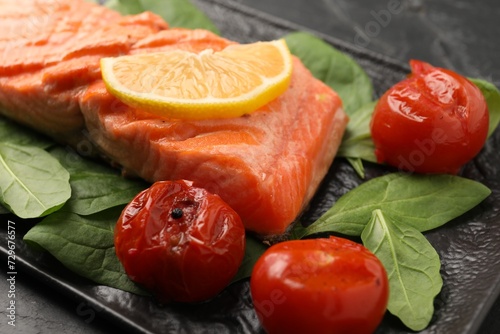 Tasty grilled salmon with tomatoes, spinach and lemon on table, closeup