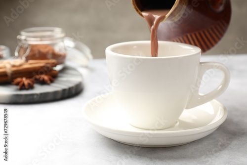 Pouring tasty hot chocolate into cup at light table, closeup. Space for text