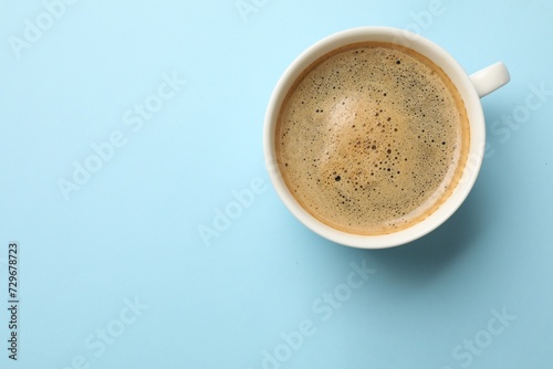 Aromatic coffee in cup on light blue background, top view. Space for text