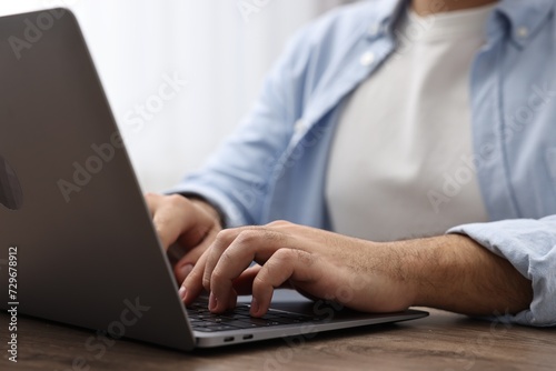 E-learning. Young man using laptop at wooden table, closeup