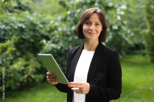 business professional woman against the backdrop of green nature. business woman with a tablet thinking, studying, counting, analyzing, looking.