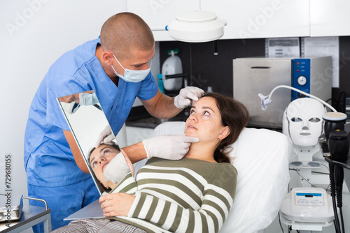 Young woman patient having consultation in aesthetic clinic, talking with confident man doctor