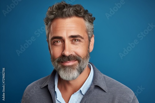 Handsome mature man looking at camera and smiling while standing against blue background