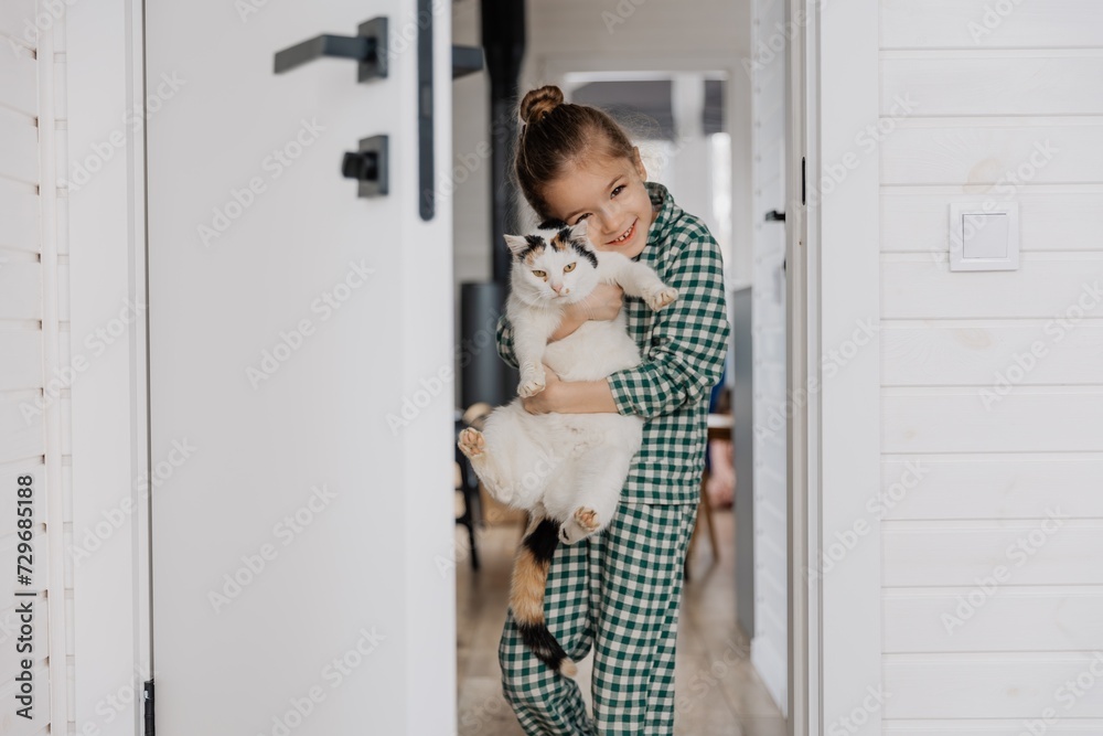 A little blond girl wearing pajamas hugs a domestic cat in her bedroom. The concept of a cozy home morning A little blond girl wearing pajamas hugs a domestic cat in her bedroom. The concept of a cozy home morning